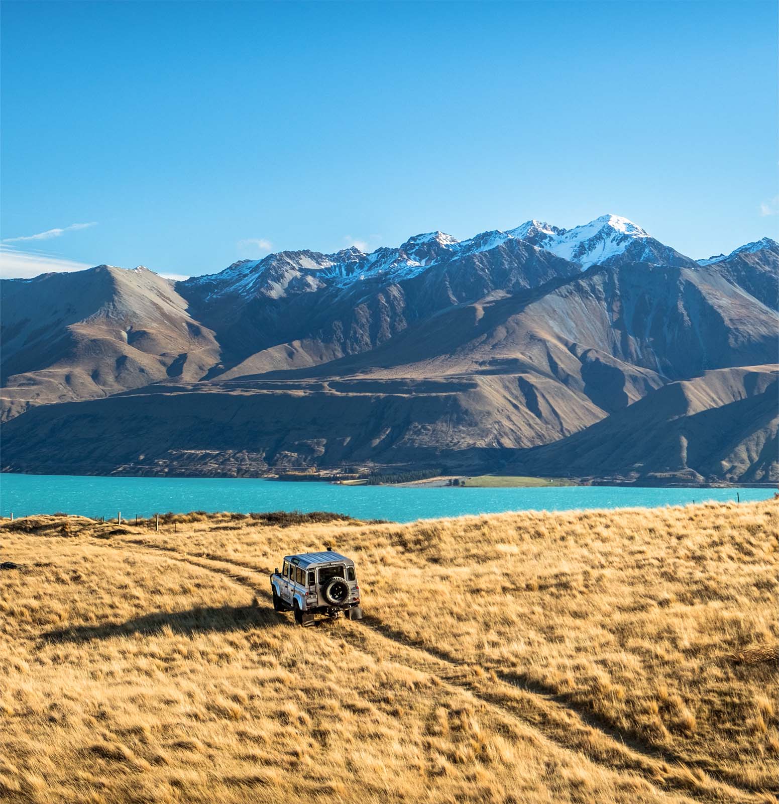 Tekapo Adventures 4WD crossing farmland toward lake with mountains in background
