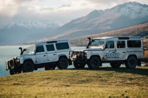 2 Land Rovers on a hillside with lake and mountians in the background