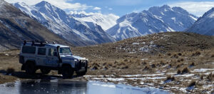Tekapo Adventures Land Rover on an icy winter tour - parked on a grassy hillside with snowy peaks in the background
