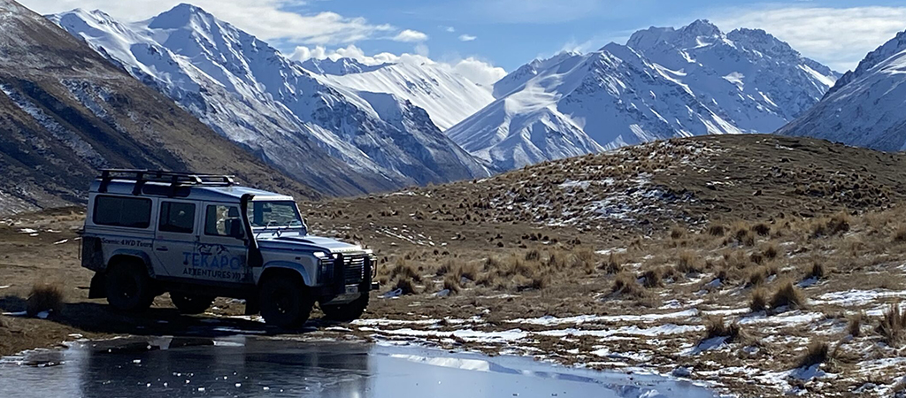 Tekapo Adventures Land Rover on an icy winter tour - parked on a grassy hillside with snowy peaks in the background